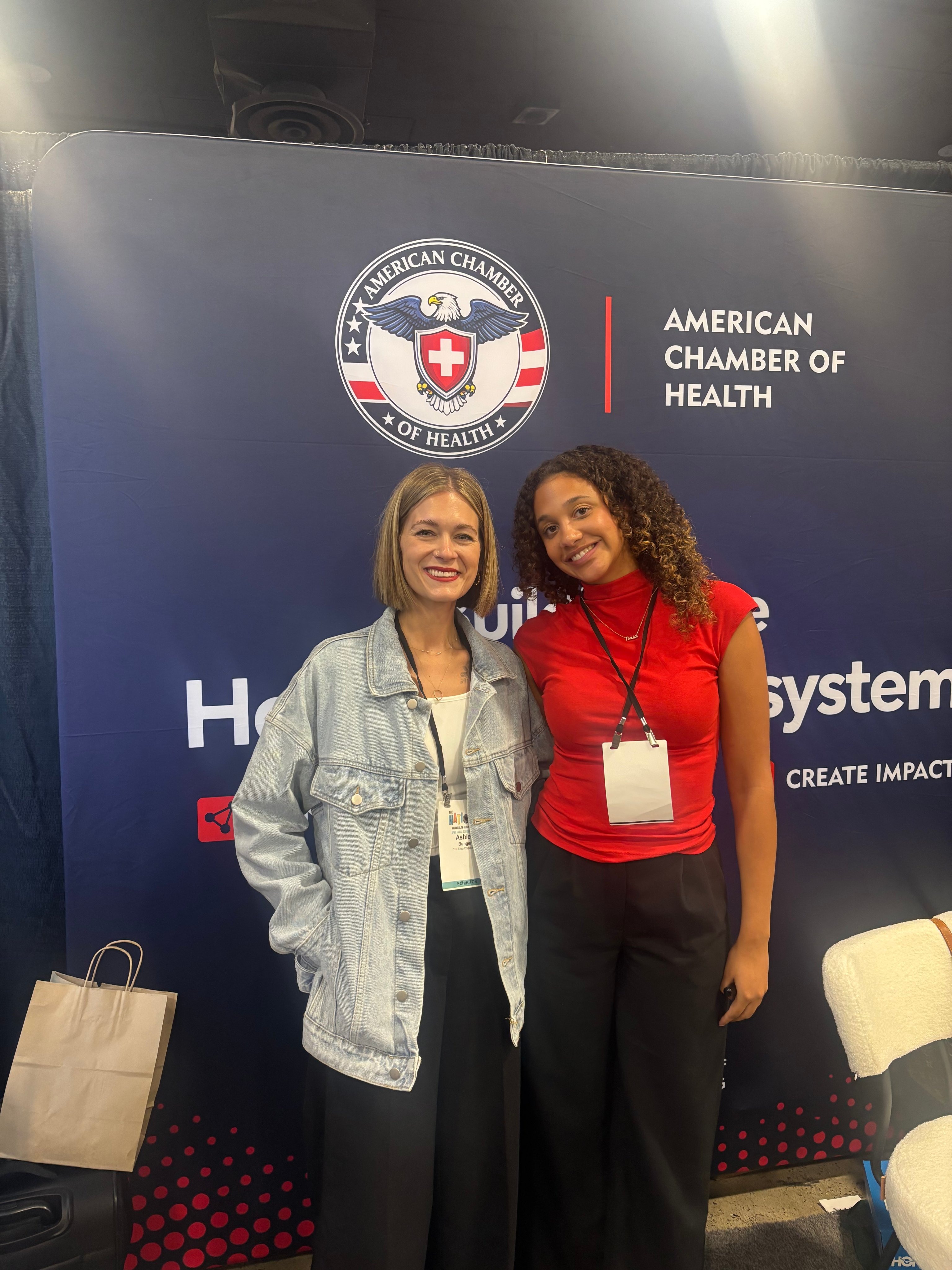 Two attendees smiling for a photo in front of the ACH backdrop