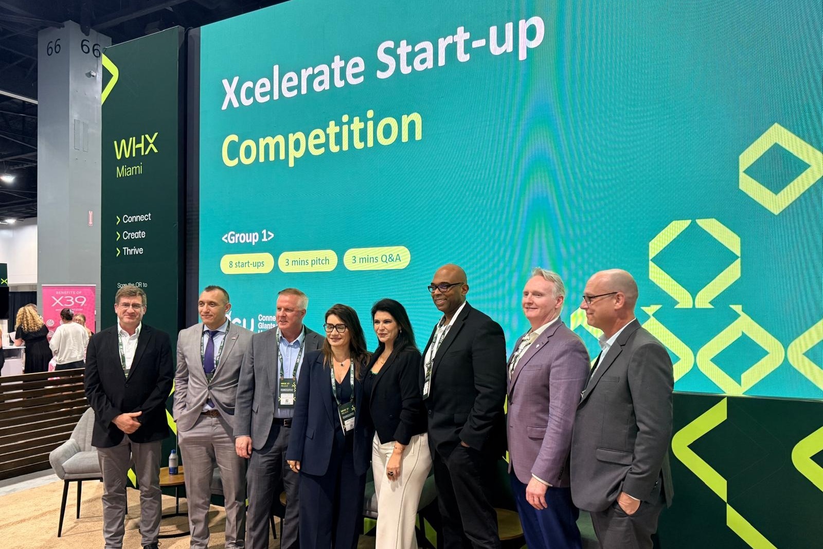 Eight healthcare founders and innovators pose before the Xcelerate Start-up Competition screen at WHX Miami