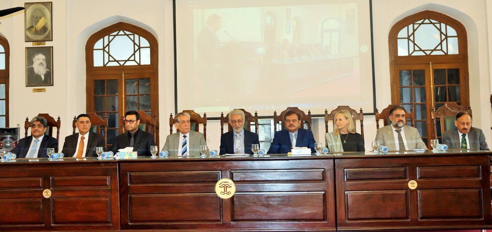 Nine panelists seated at the dais table in the KEMU hall